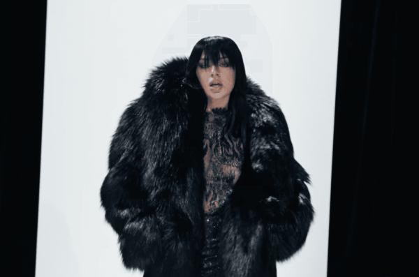 Charli XCX walks the runway in a black fauxfur coat lace top and long hair styled with bangs.